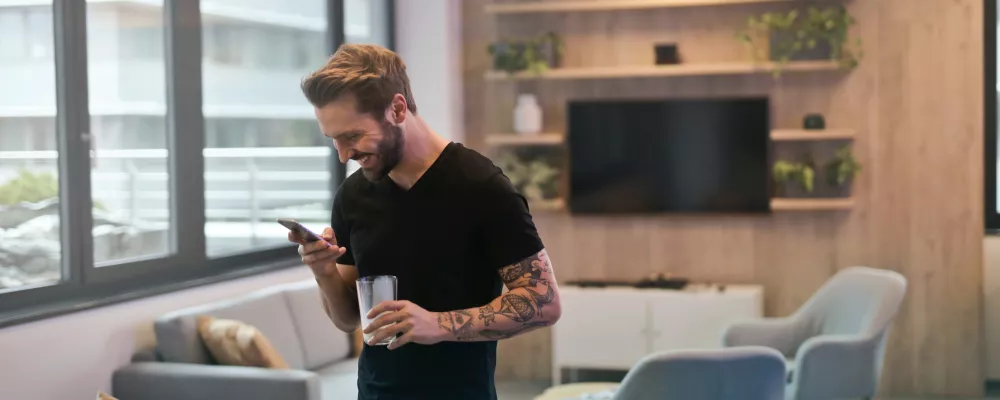 Ein Mann blickt lachend auf sein Mobiltelefon