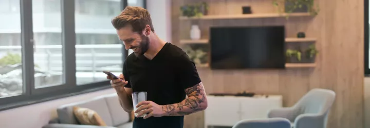 Ein Mann blickt lachend auf sein Mobiltelefon